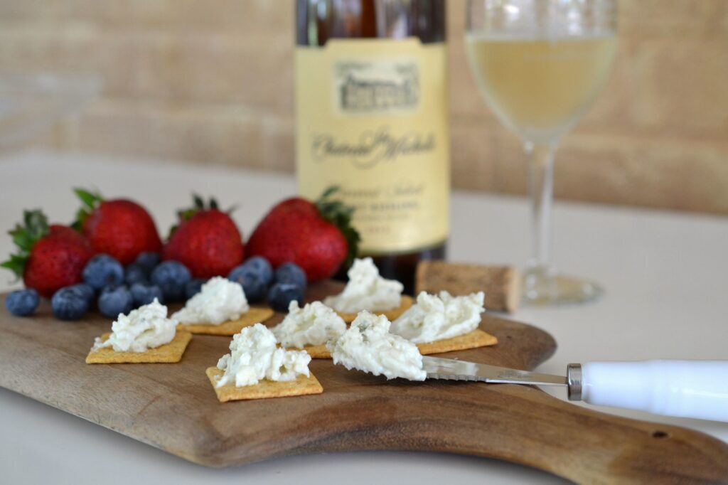 A tray of cheese spread on crackers with fruit and wine.